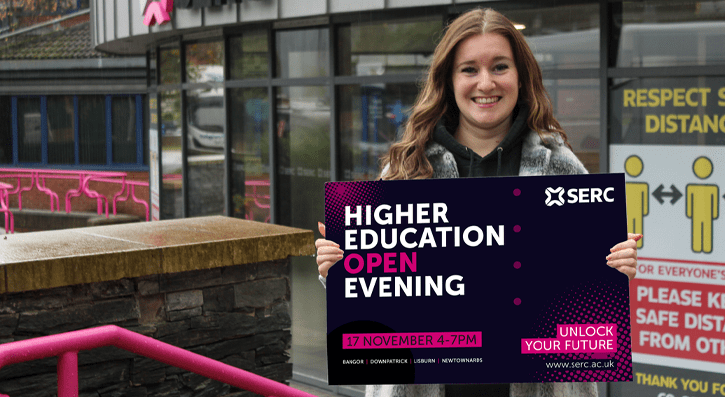 HE Student Zara Shaw outside Bangor Campus holding a board to promote HE Open Evening 